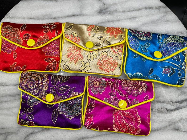 May include: Six small, colourful pouches with floral patterns and yellow trim. Each pouch has a yellow button closure.