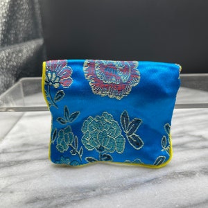 May include: A small blue pouch with a floral pattern and yellow trim. The pouch is made of a soft, silky fabric.