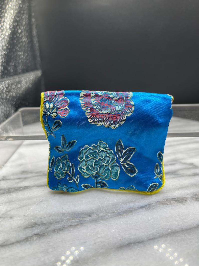 May include: A small blue pouch with a floral pattern and yellow trim. The pouch is made of a soft, silky fabric.