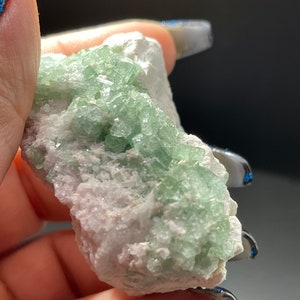 May include: A cluster of green crystals on a white matrix. The crystals are small and have a glassy lustre. The matrix is rough and has a white colour.