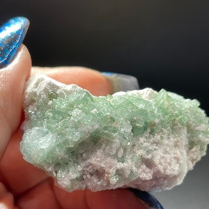 May include: A cluster of green crystals on a white matrix. The crystals are small and have a glassy lustre. The matrix is rough and has a white colour.