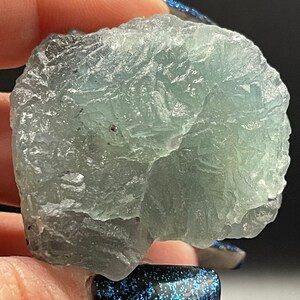 May include: A light green fluorite crystal with a rough, textured surface. The crystal has a translucent appearance and shows signs of natural formation.