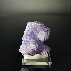 Peut inclure: Un cristal de fluorine violet avec une structure cubique. Le cristal est sur un support d'exposition blanc.