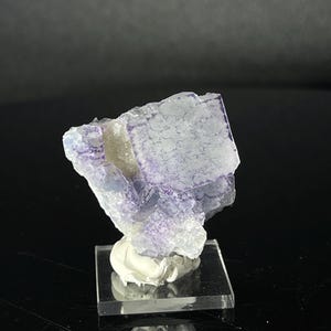 Peut inclure: Un spécimen de cristal de fluorine violet sur un support d'exposition transparent. Le cristal a une apparence translucide et vitreuse avec une teinte violette.