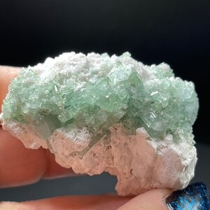 May include: A cluster of green crystals embedded in a white matrix. The crystals are translucent and have a glassy lustre. The matrix is rough and textured.