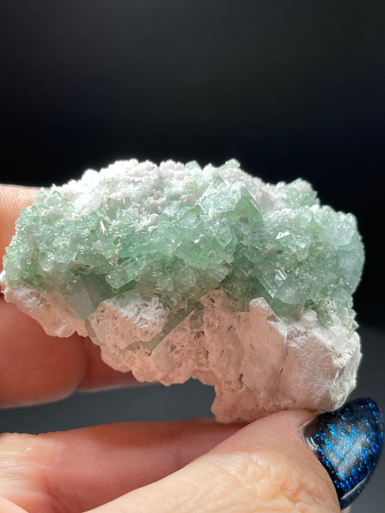 May include: A cluster of green crystals embedded in a white matrix. The crystals are translucent and have a glassy lustre. The matrix is rough and textured.