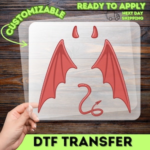 May include: A DTF transfer featuring a red devil wing, tail, and horn design. The words "CUSTOMIZABLE" and "READY TO APPLY" are printed on the transfer. The image also includes the text "NEXT DAY SHIPPING".