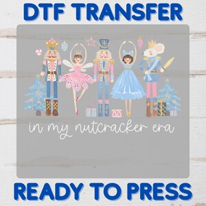 May include: A DTF transfer design featuring illustrations of nutcracker figures, a ballerina, and a mouse king, with the text "in my nutcracker era." The design includes Christmas trees and gift boxes, with the words "READY TO PRESS" at the bottom.