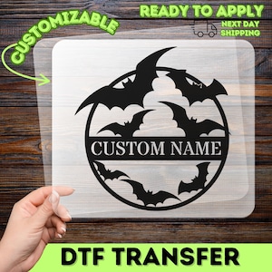 May include: A black circular decal featuring a silhouette design of multiple flying bats arranged around a central horizontal bar with the text CUSTOM NAME printed in a bold, sans-serif font. The graphic is displayed on a clear backing sheet.