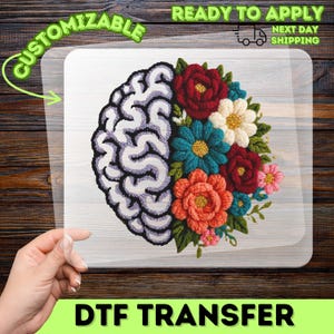 May include: A DTF transfer featuring a brain design on the left and colorful embroidered flowers on the right. The brain is white and purple, and the flowers are red, orange, teal, and white. The text "CUSTOMIZABLE" and "DTF TRANSFER" are also visible.