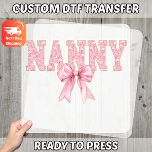 May include: A white DTF transfer sheet with the word "NANNY" in pink floral letters and a pink bow. The text "CUSTOM DTF TRANSFER" and "READY TO PRESS" are at the top and bottom. An orange and white icon indicates next day shipping.
