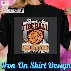 May include: Black t-shirt with a basketball-themed graphic. The design features the words "Rivervale Fireball Shooters" with a basketball and flames. The text "Light Up The Game" is also included. The words "Do It Yourself" and "Iron-On Shirt Design" are also visible.