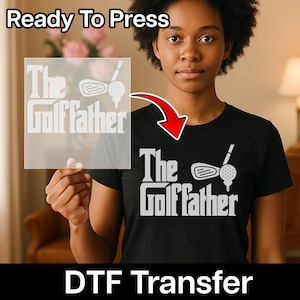 May include: Black t-shirt with the text "The Golf Father" in white, along with a golf club and ball graphic. The image also shows a DTF transfer with the same design, and the words "Ready To Press".