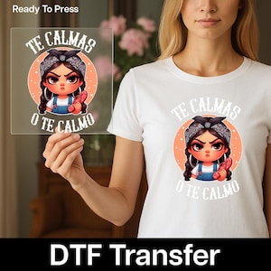May include: White t-shirt featuring a cartoon illustration of a girl with a bandana, hoop earrings, and overalls, holding a red object. The text "TE CALMAS O TE CALMO" is above and below the image. The words "Ready To Press" and "DTF Transfer" are also visible.
