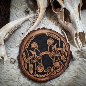 May include: A wooden round disc with a black background and a brown intricate design of a knotwork pattern. The design is reminiscent of a Celtic knot.
