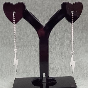 May include: A pair of silver earrings with a lightning bolt charm hanging from a delicate chain.