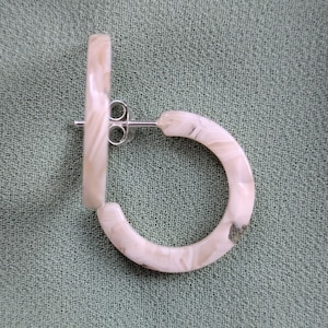 May include: A pair of white hoop earrings with a marbled pattern. The earrings are made of a lightweight material and have a silver post.