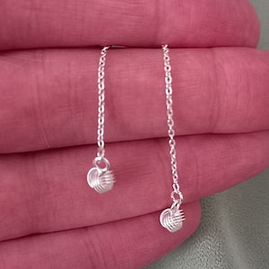 May include: A pair of silver dangle earrings with a twisted wire design. The earrings are hanging from a delicate chain.