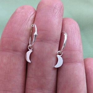 May include: A pair of silver hoop earrings with a crescent moon charm hanging from each hoop.