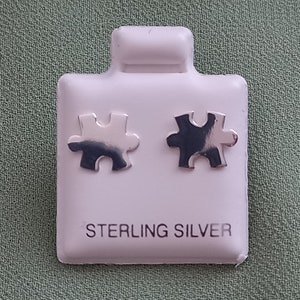 May include: A pair of sterling silver puzzle piece earrings on a white display card.