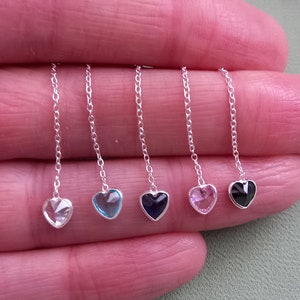 May include: Five silver chains with heart-shaped charms. The charms are clear, light blue, dark blue, pink, and black.