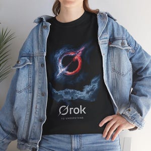 May include: Black t-shirt with a graphic design. The design features a red and white circular shape with a line through it, set against a dark blue and grey cloudy background. The text "Ørok TO UNDERSTAND" is printed below.