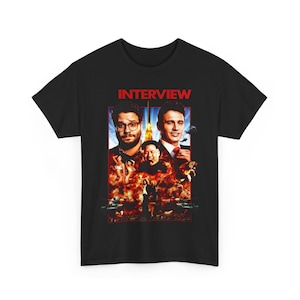 May include: Black t-shirt featuring a movie poster design with the word "INTERVIEW" in red. The poster includes images of two men, explosions, and other figures. A graphic tee for movie fans.
