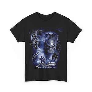 Può includere: T-shirt nera con grafica del film "Alien vs. Predator". Il design presenta i personaggi Predator e Alien, con il titolo del film "AVP" in lettere argentate. Lo sfondo è blu scuro.