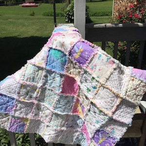 May include: A patchwork quilt made of various fabrics in shades of pink, purple, blue, and white. The quilt is made of squares and has a frayed edge.