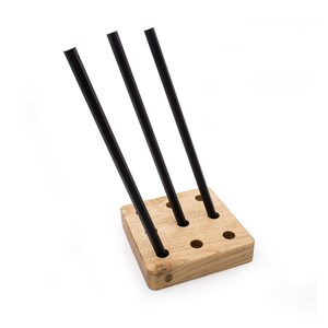 May include: A wooden stand with multiple holes to hold black metal rods. The stand is made of light brown wood and has a square shape.