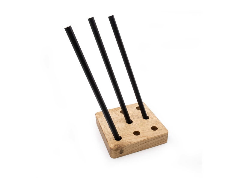 May include: A wooden stand with multiple holes to hold black metal rods. The stand is made of light brown wood and has a square shape.