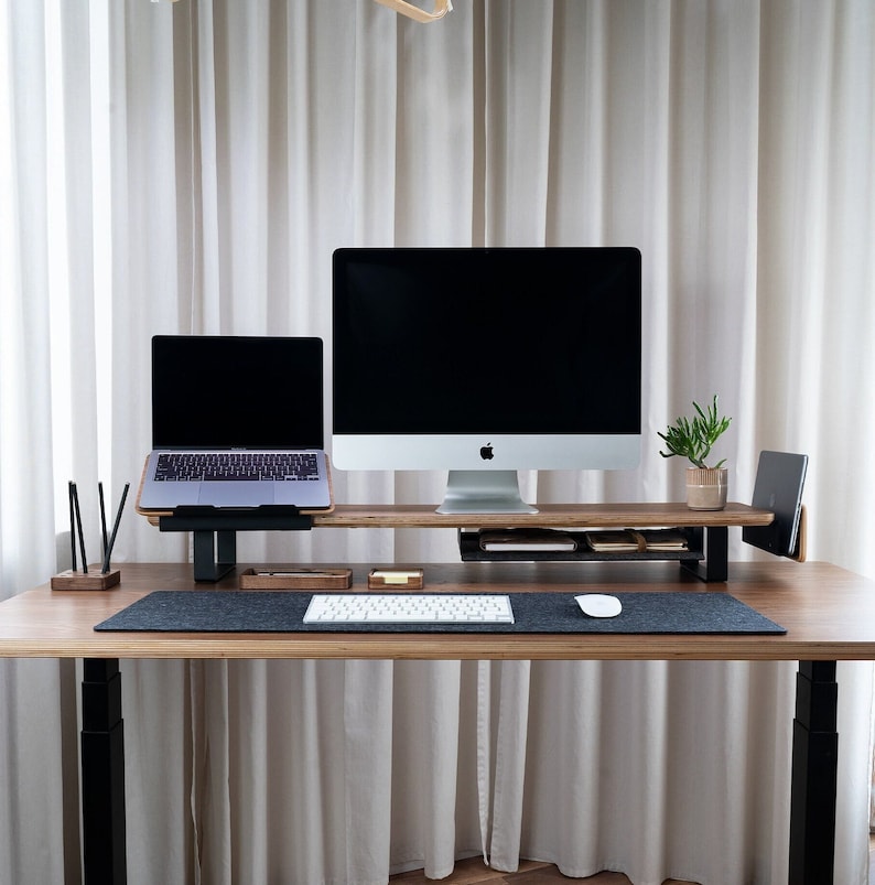 May include: A black laptop and a desktop computer are on a wooden stand with a keyboard and mouse on a desk. The desk is black and has a white surface. There is a plant in a pot on the stand.