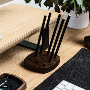 May include: A dark brown wooden pencil holder with six slots for pencils. The holder is on a wooden desk with a black mouse mat and a white keyboard.