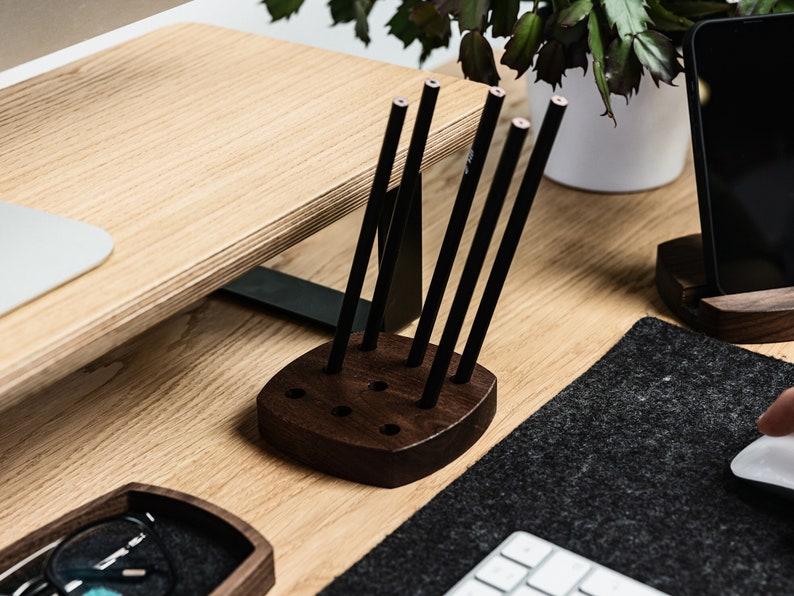 May include: A dark brown wooden pencil holder with six slots for pencils. The holder is on a wooden desk with a black mouse mat and a white keyboard.