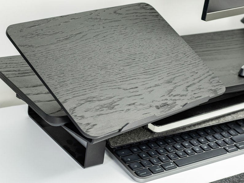 May include: A black wooden laptop stand with a tilting top. The stand is adjustable and can be raised or lowered to different heights. The stand is made of a durable material and is designed to support the weight of a laptop.