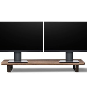 Pu&ograve; includere: Due monitor per computer neri con cornici sottili sono montati su un supporto in legno con gambe in metallo. Il supporto &egrave; marrone con una finitura in legno naturale.