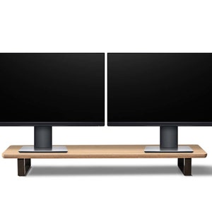 Pu&ograve; includere: Due monitor per computer neri con cornici sottili sono montati su un supporto in legno con gambe in metallo nero. Il supporto &egrave; su una superficie bianca.