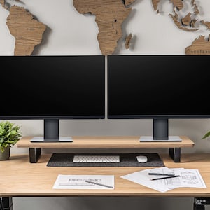 Pu&ograve; includere: Due monitor per computer neri sono montati su un supporto in legno. I monitor sono posizionati su una scrivania in legno chiaro con una tastiera, un mouse e dei fogli. Una piccola pianta verde &egrave; sulla scrivania a sinistra dei monitor. Una mappa del mondo in legno &egrave; sul muro dietro i monitor.