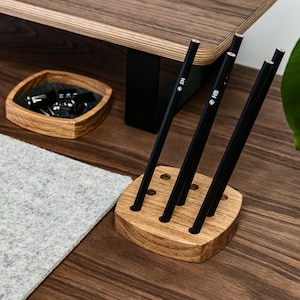 May include: A wooden pencil holder with six slots, holding five black pencils. The pencils are labelled with the grades "2H" and "HB".