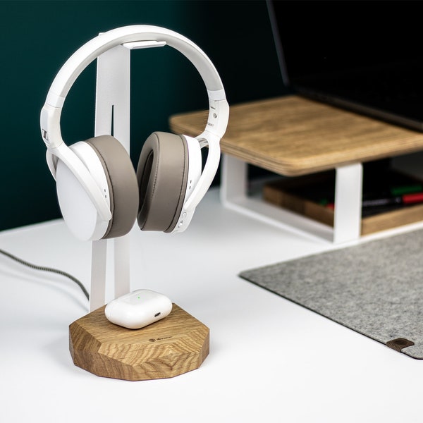 May include: White headphones with a gray earcup on a white stand with a wooden base. A white wireless charging case is on the base.