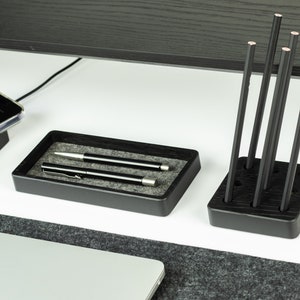 May include: Black wooden desk organiser with two compartments. One compartment holds two silver pens and the other holds six black pencils.