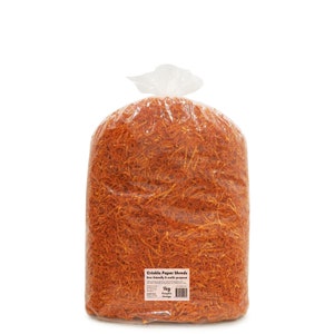 Op de afbeelding: Een grote zak met oranje gekreukelde papieren stroken. De zak is van doorzichtig plastic en de papieren stroken zijn fel oranje. De zak is gelabeld met "Crinkle Paper Shreds Eco-friendly & multi-purpose 1kg Pumpkin Orange".