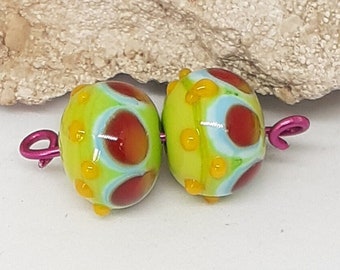 Dos cuentas de vidrio, verde claro, azul claro, rojo y amarillo anaranjado para joyería o pasatiempos creativos.