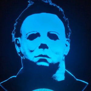 May include: A blue light-up 3D sculpture of Michael Myers, the iconic horror movie character, with a white mask and a detailed face. The sculpture is lit from the bottom, casting a blue glow on the face.