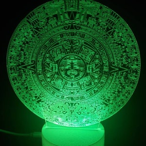 Op de afbeelding: Een groen acryl nachtlampje in de vorm van de Azteekse kalender, ook wel bekend als de Zonnesteen. Het licht is aan en verlicht de ingewikkelde gravures op de steen.