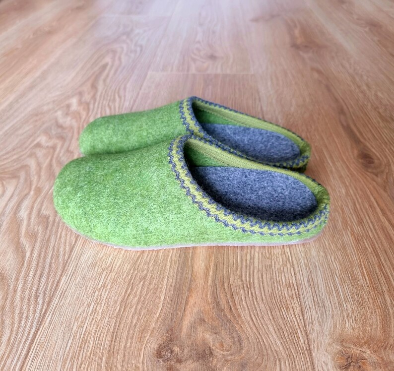 Puede incluir: Un par de zapatillas de fieltro verde con interiores grises y ribetes decorativos. Las zapatillas est&aacute;n hechas de un material suave y texturizado y est&aacute;n dise&ntilde;adas para uso en interiores. Miden unos 25 cm de largo.