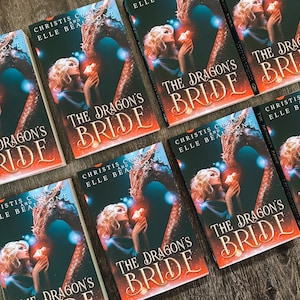 Op de afbeelding: Een stapel paperbacks met een fantasythema. De omslagen tonen een draak en een vrouw met blond haar. De titel van het boek is "The Dragon's Bride".