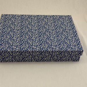 May include: A rectangular lidded box featuring a deep blue and white intricate floral scrollwork pattern across the top and sides. The box has a structured shape with sharp corners and a flat lid that sits flush with the base of the container.