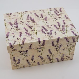 Könnte beinhalten: Eine rechteckige Schachtel mit Deckel, verziert mit einem Lavendel-Blumenmuster. Das Design zeigt lila Lavendelzweige auf cremefarbenem Hintergrund mit dezentem Schriftzug. Ideal für Aufbewahrung oder zum Verschenken.