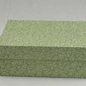 Può includere: Una scatola regalo rettangolare con un motivo floreale verde chiaro. La scatola ha un coperchio e una base, entrambi ricoperti da un motivo ripetuto di piccoli fiori e foglie bianche. La scatola è adatta per i regali.